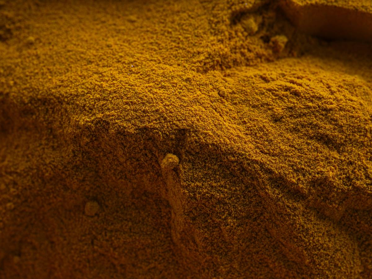 Golden turmeric powder in a wooden bowl next to whole turmeric roots—a natural herbal aid for digestion